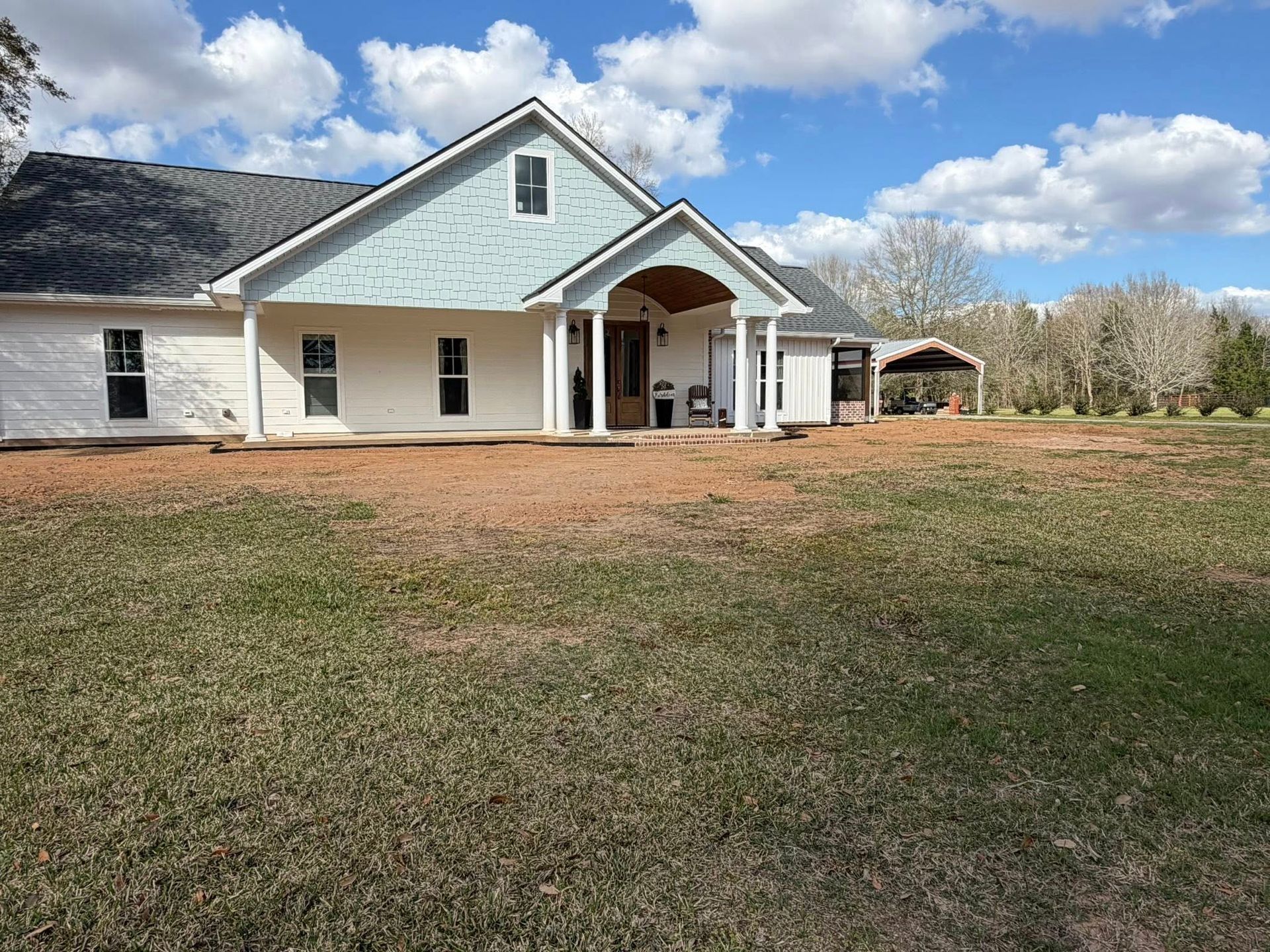 Single-story house with white siding, blue gable, and a large front yard under a partly cloudy sky