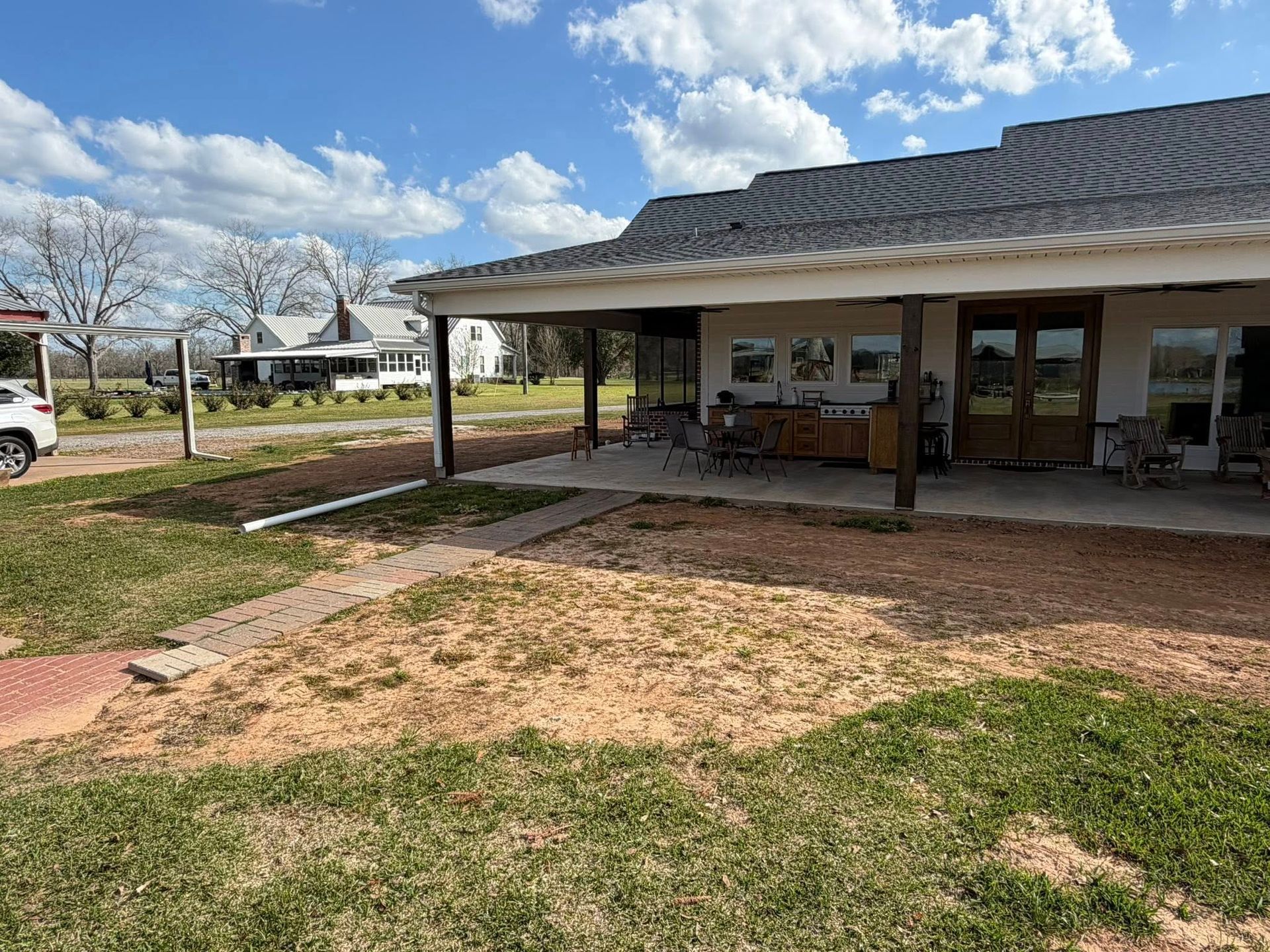 Rural house with a covered porch, white columns, and a dirt patch in the yard under a cloudy sky