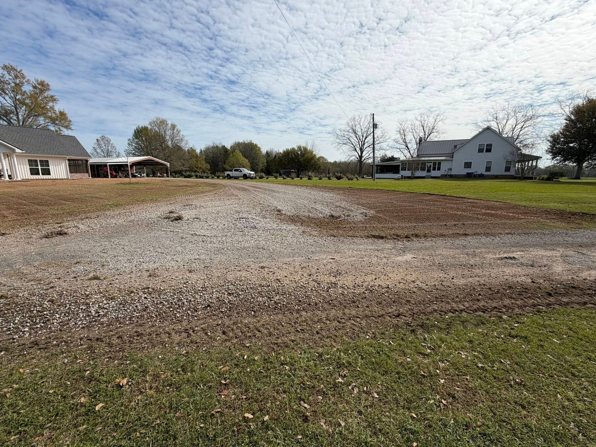 Gravel lot beside suburban houses and lawn under a partly cloudy sky