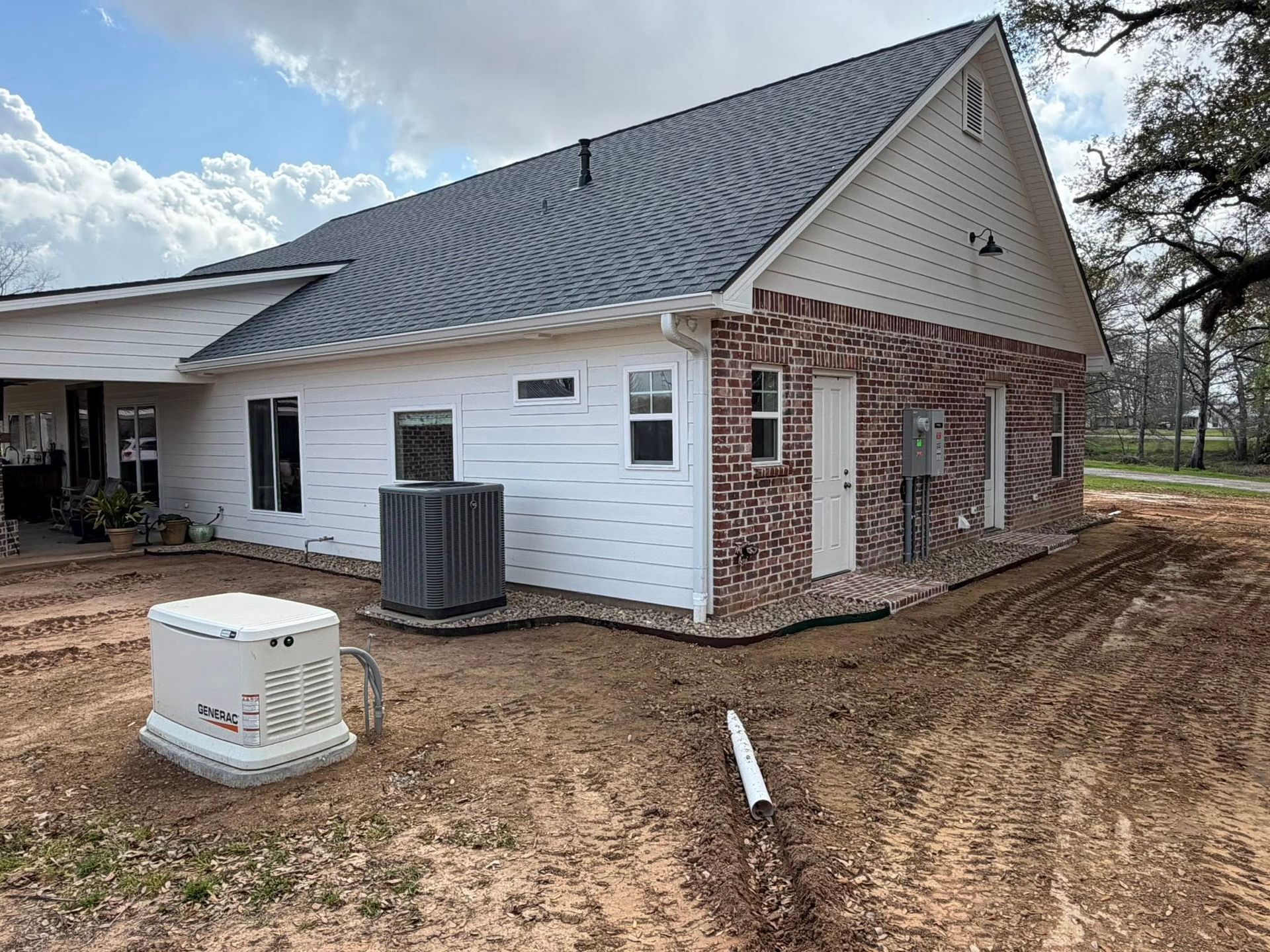 Side of a white brick house under construction with HVAC unit and dirt yard