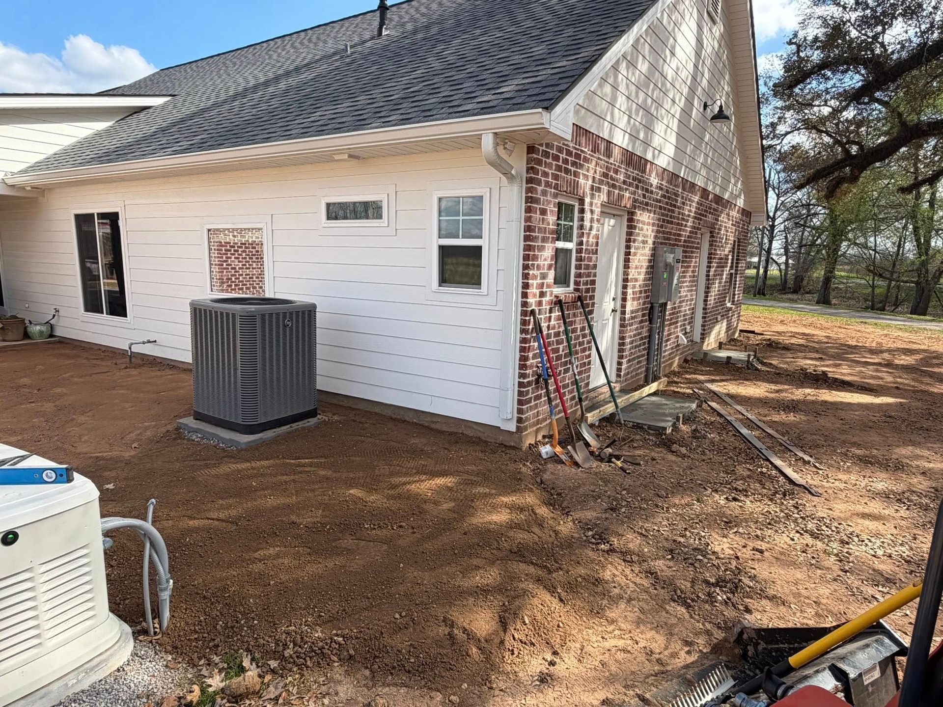 White house exterior with brick and siding, HVAC units, and a wooded yard on the right