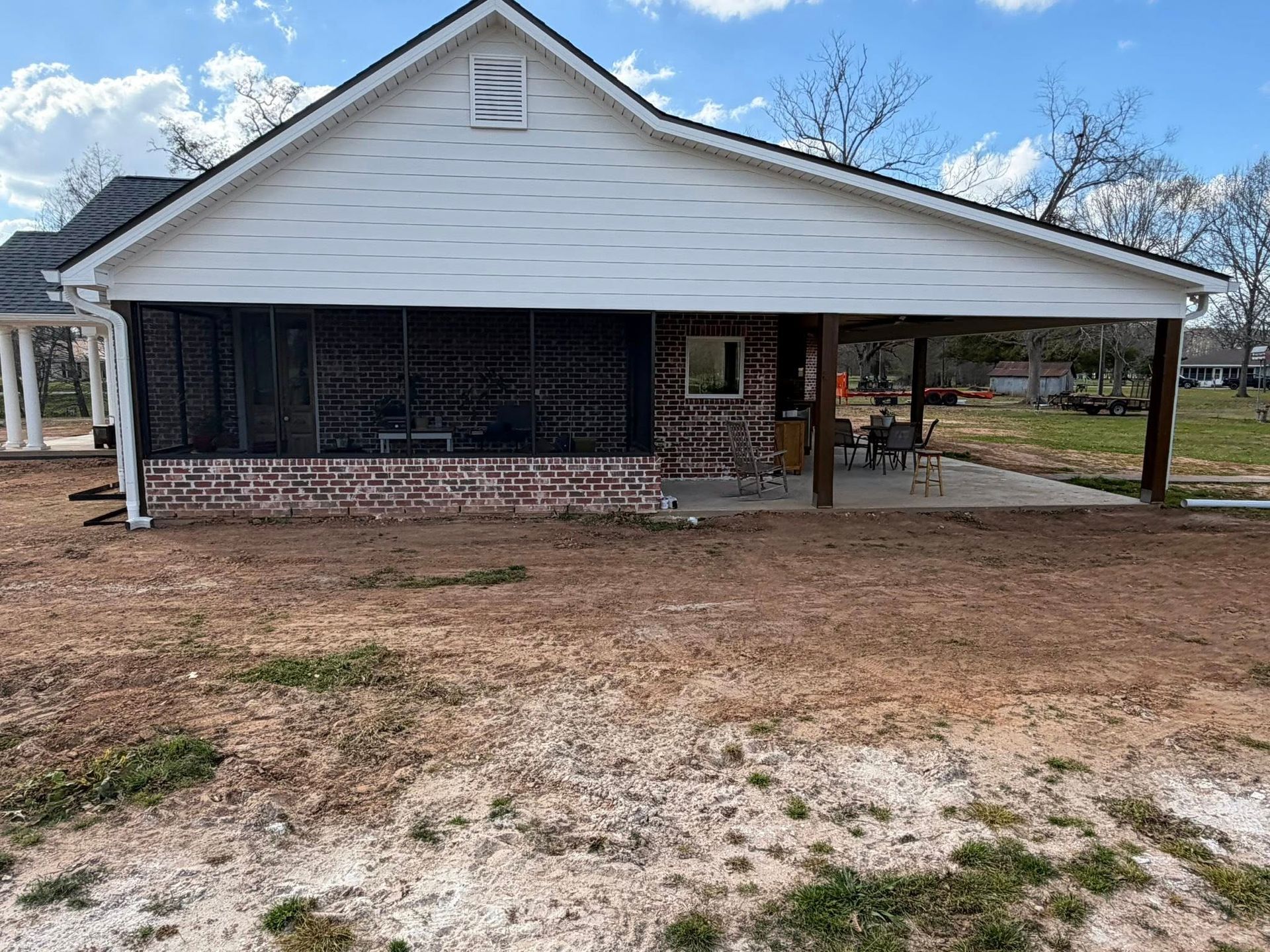 Single-story white house with brick porch, screened front, and a carport on a dirt yard.
