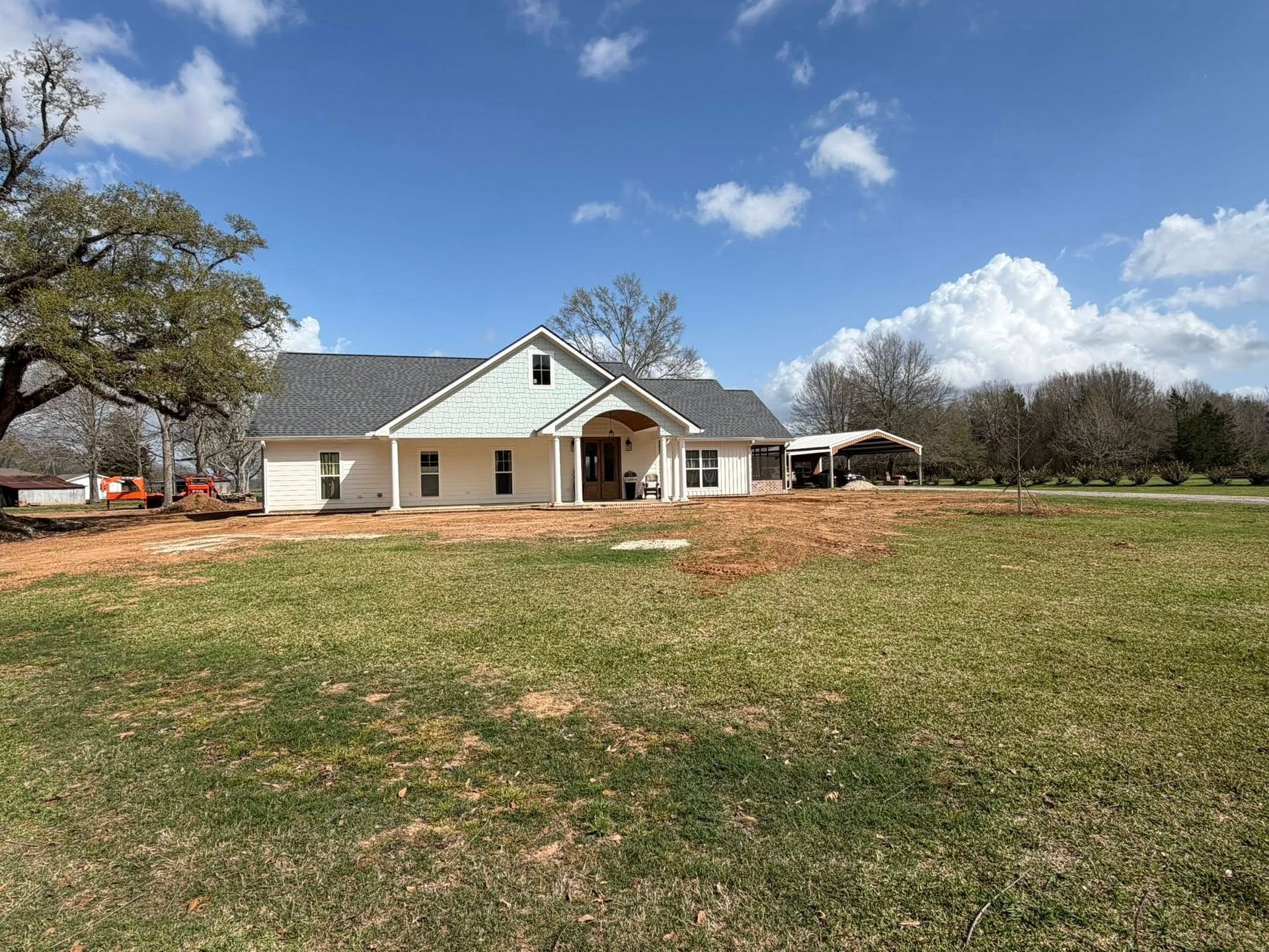 Single-story beige house with a covered porch on a large grassy lot under a blue sky