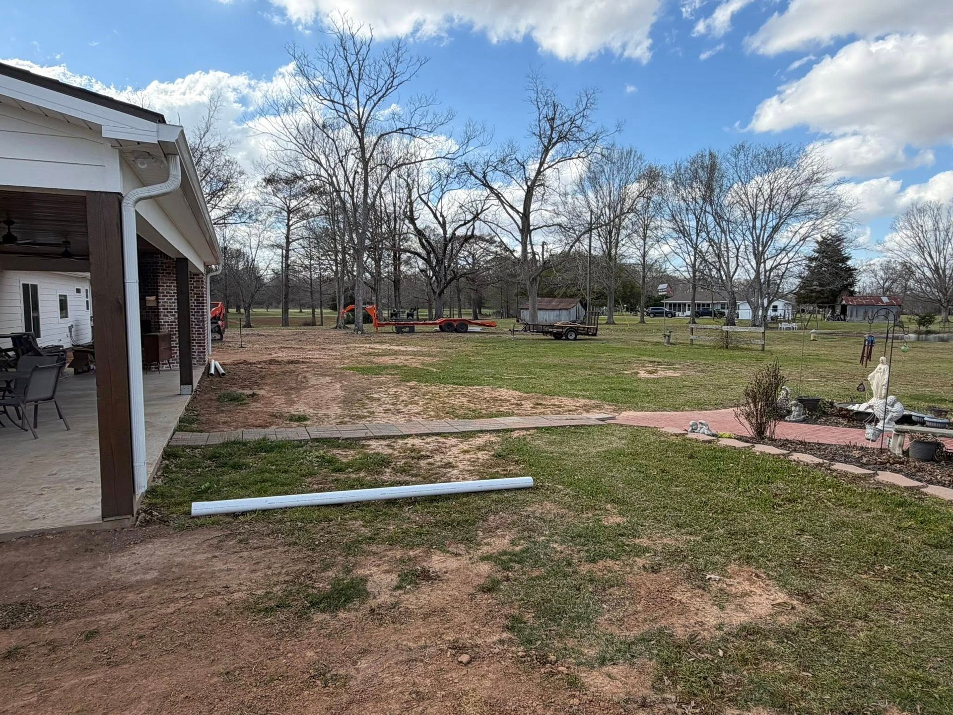 Backyard with patchy grass, bare trees, a porch, and a small fountain under a partly cloudy sky