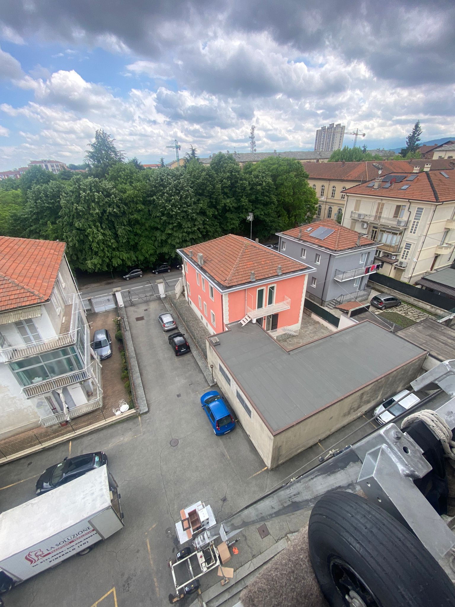 Vista dall'alto di una strada cittadina con edifici, auto parcheggiate e un cielo azzurro con nuvole.
