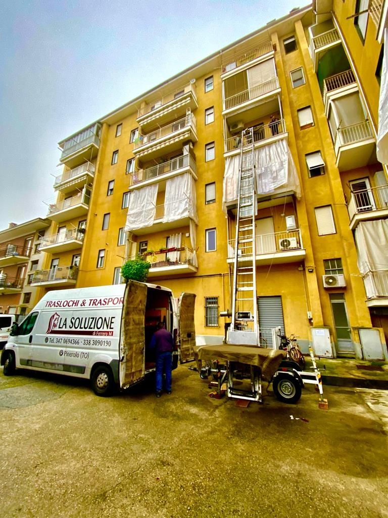 Camion per traslochi con piattaforma elevatrice che scarica oggetti da un condominio giallo.