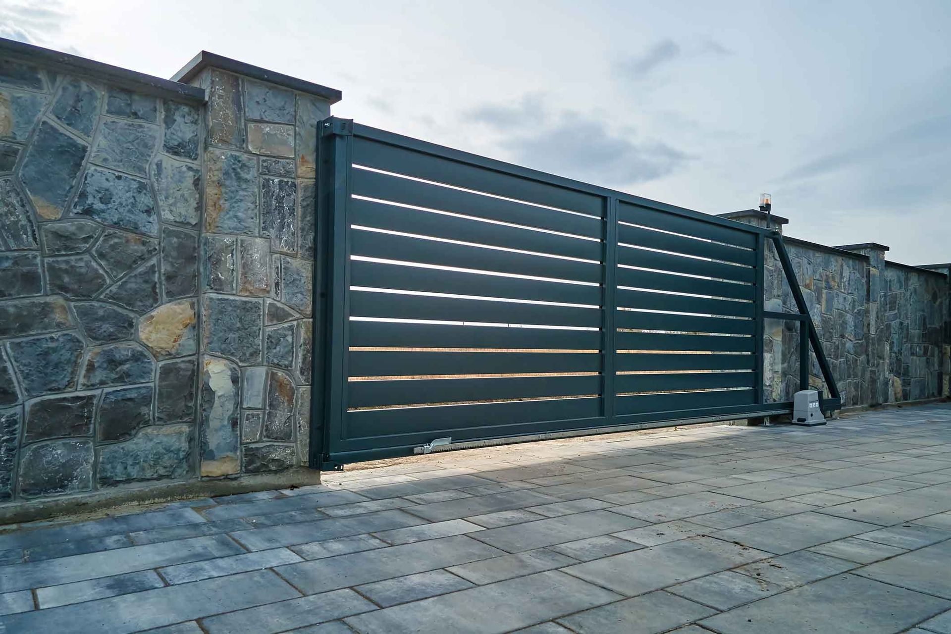 A black sliding gate is sitting in front of a stone wall.