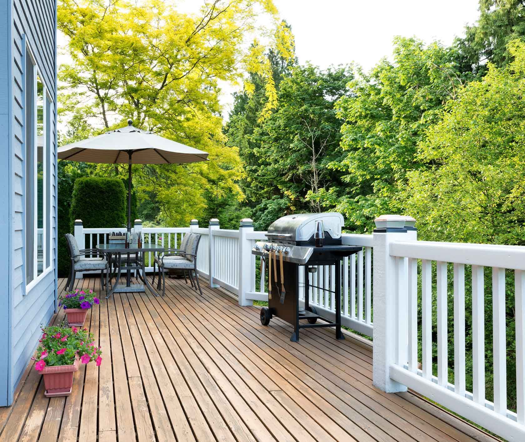 A Wooden Deck With A Grill And Umbrella On It – Mishawaka IN - Milestone Fence
