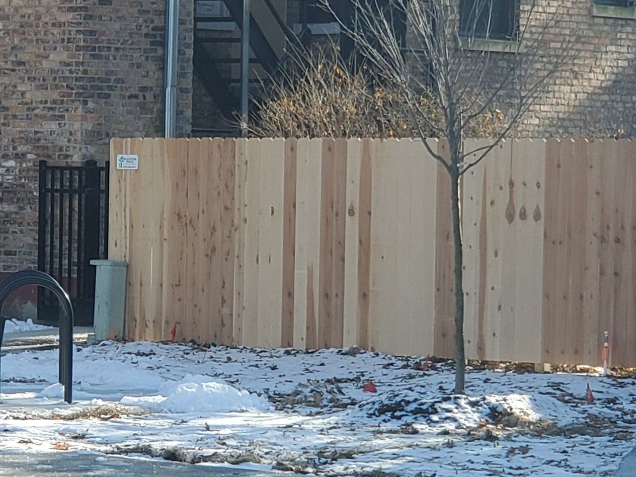 A Wooden Fence Is In Front Of A Brick Building – Mishawaka IN - Milestone Fence