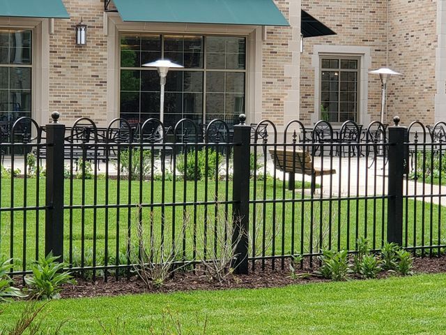 A Black Fence Surrounds A Lush Green Lawn In Front Of A Brick Building – Mishawaka IN - Milestone Fence