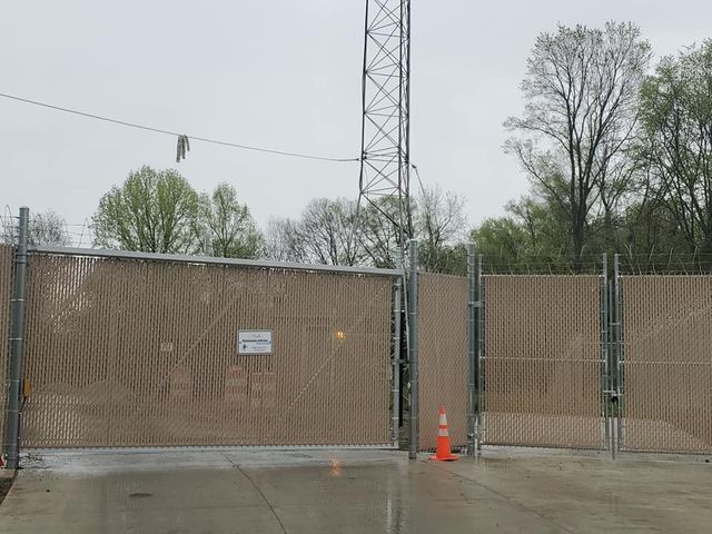 A Chain Link Fence Is Surrounding A Parking Lot With Trees In The Background – Mishawaka IN - Milestone Fence