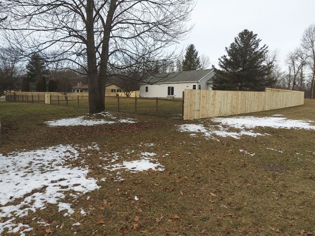 A Wooden Fence Surrounds A Grassy Yard With A House In The Background – Mishawaka IN - Milestone Fence