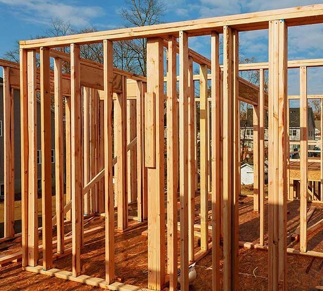 Wooden framing for the walls of a residential building under construction against a clear blue sky.