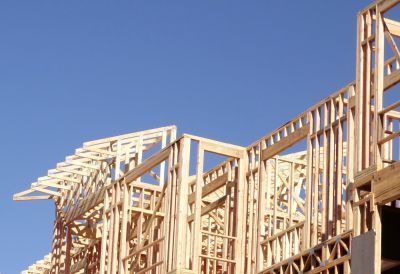 A low-angle view of a wooden house frame under construction against a clear blue sky.