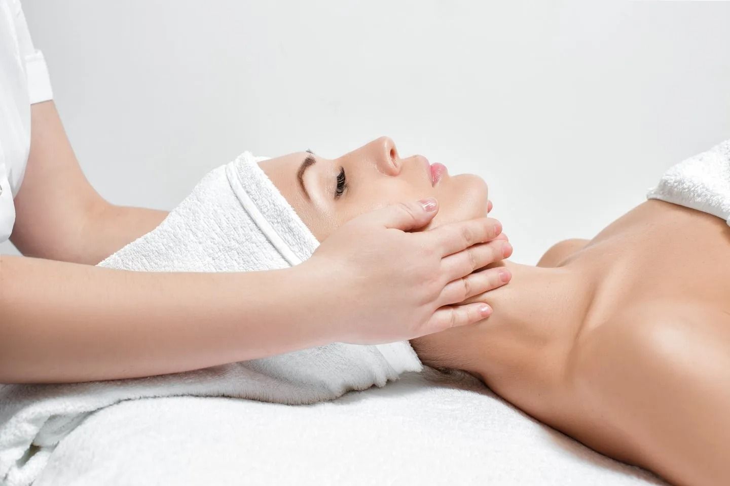 Spa therapist giving a facial massage to a reclining client with a towel on the head
