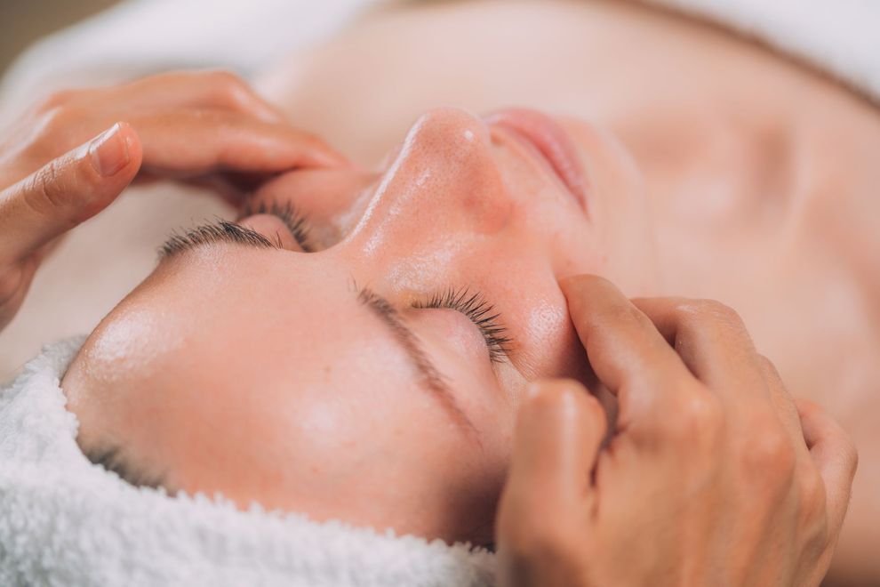 Hands giving a facial massage to a relaxed person with eyes closed, lying on a towel.