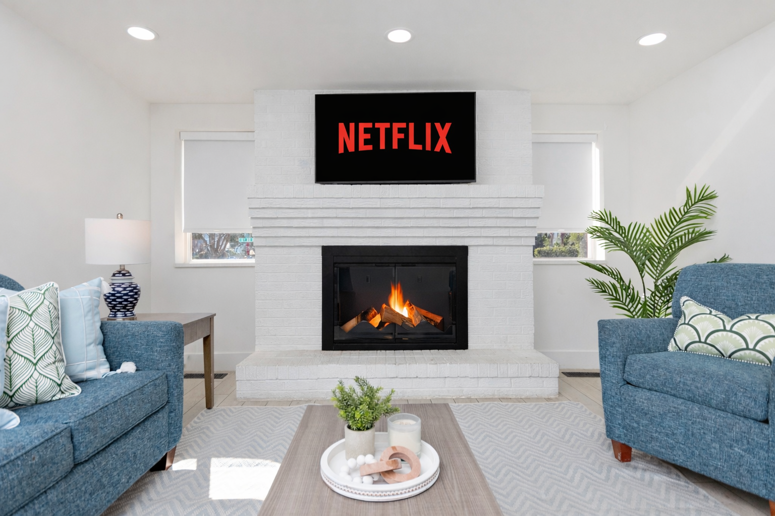 Modern living room with a lit fireplace and a TV displaying Netflix between two blue sofas