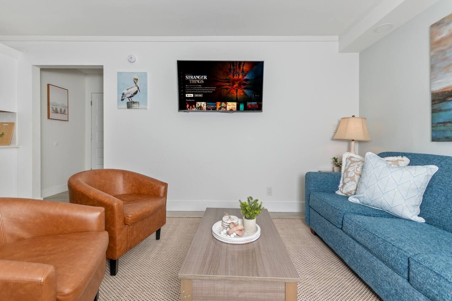 Modern living room with blue sofa, tan chairs, coffee table, and wall-mounted TV