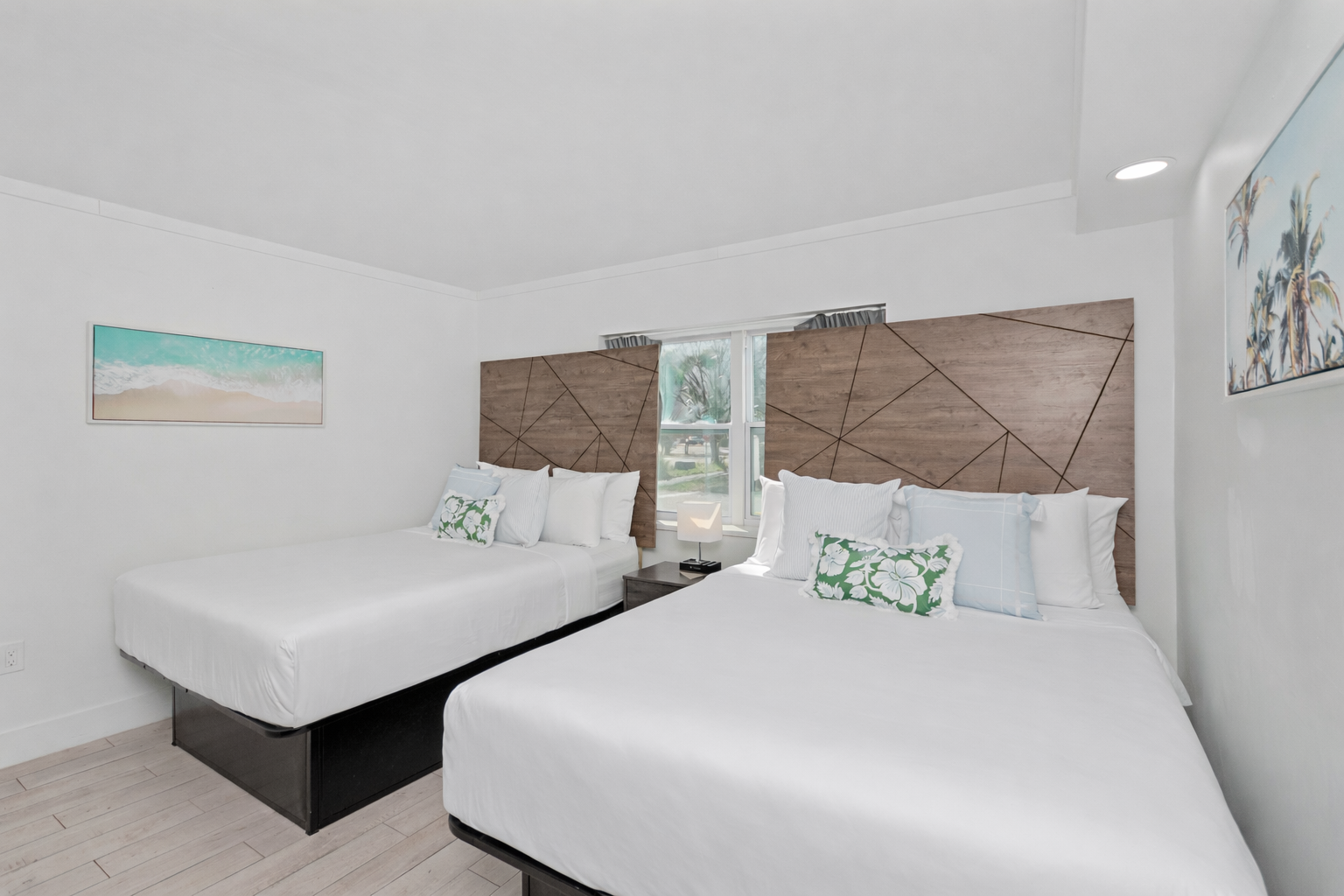 Bright twin bedroom with two white beds, woven headboards, and a small window between them