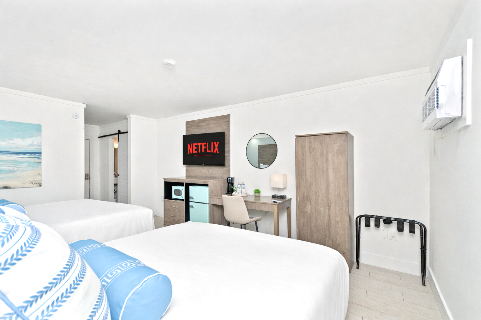 Bright white hotel room with twin beds, TV, wardrobe, and a small desk area