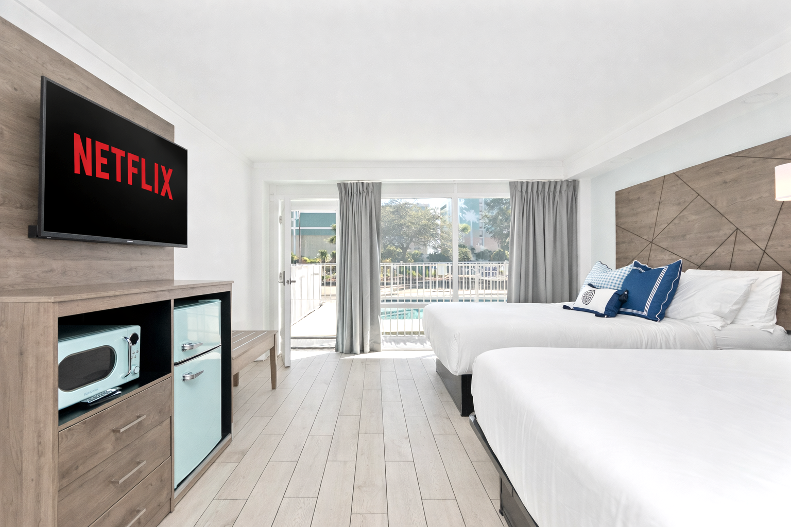 Modern hotel room with two white beds, TV, mini fridge, and balcony view