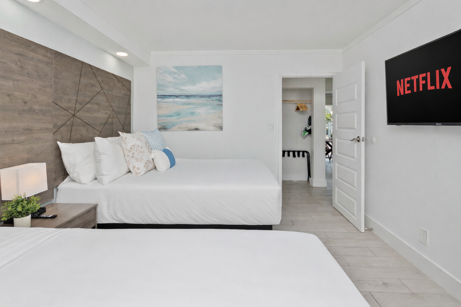 Bright hotel bedroom with a bed, nightstand, wall art, and a TV displaying Netflix.