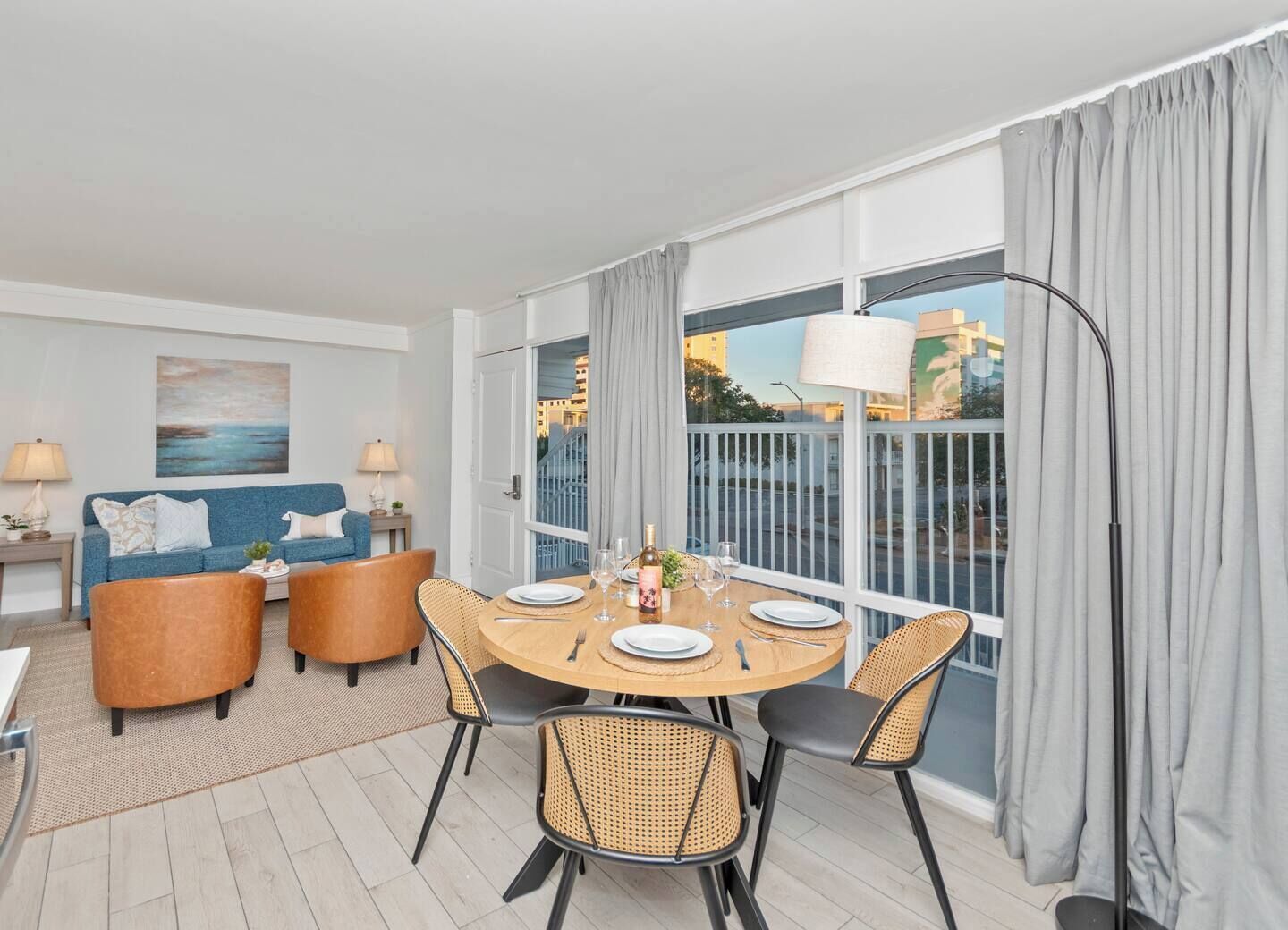 Bright dining and living room with wicker chairs, blue sofa, and large sliding doors to a balcony