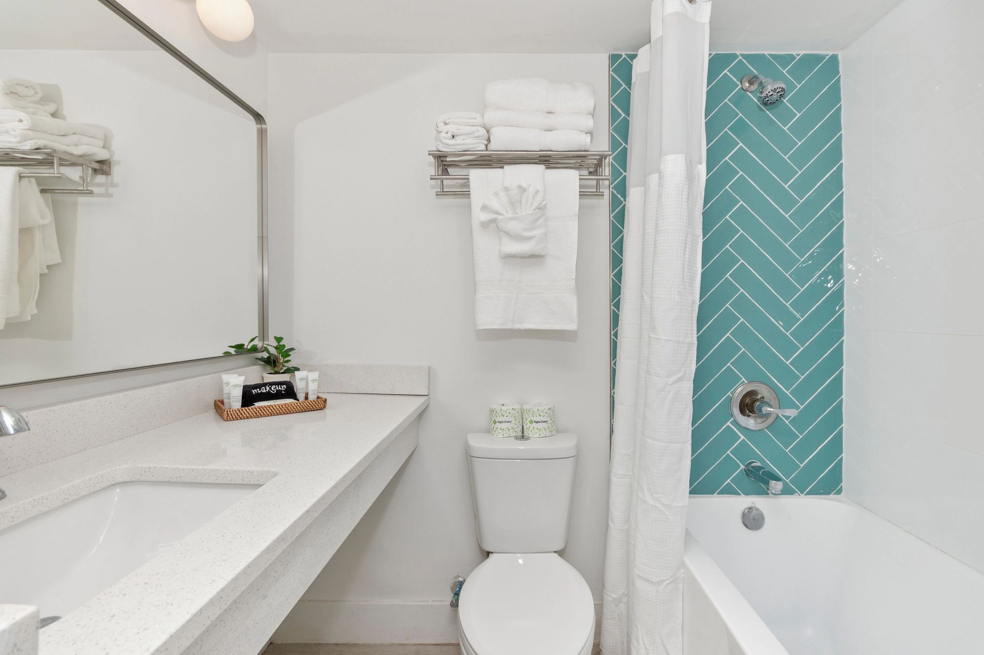Bright white bathroom with vanity, toilet, and bathtub with teal patterned shower curtain