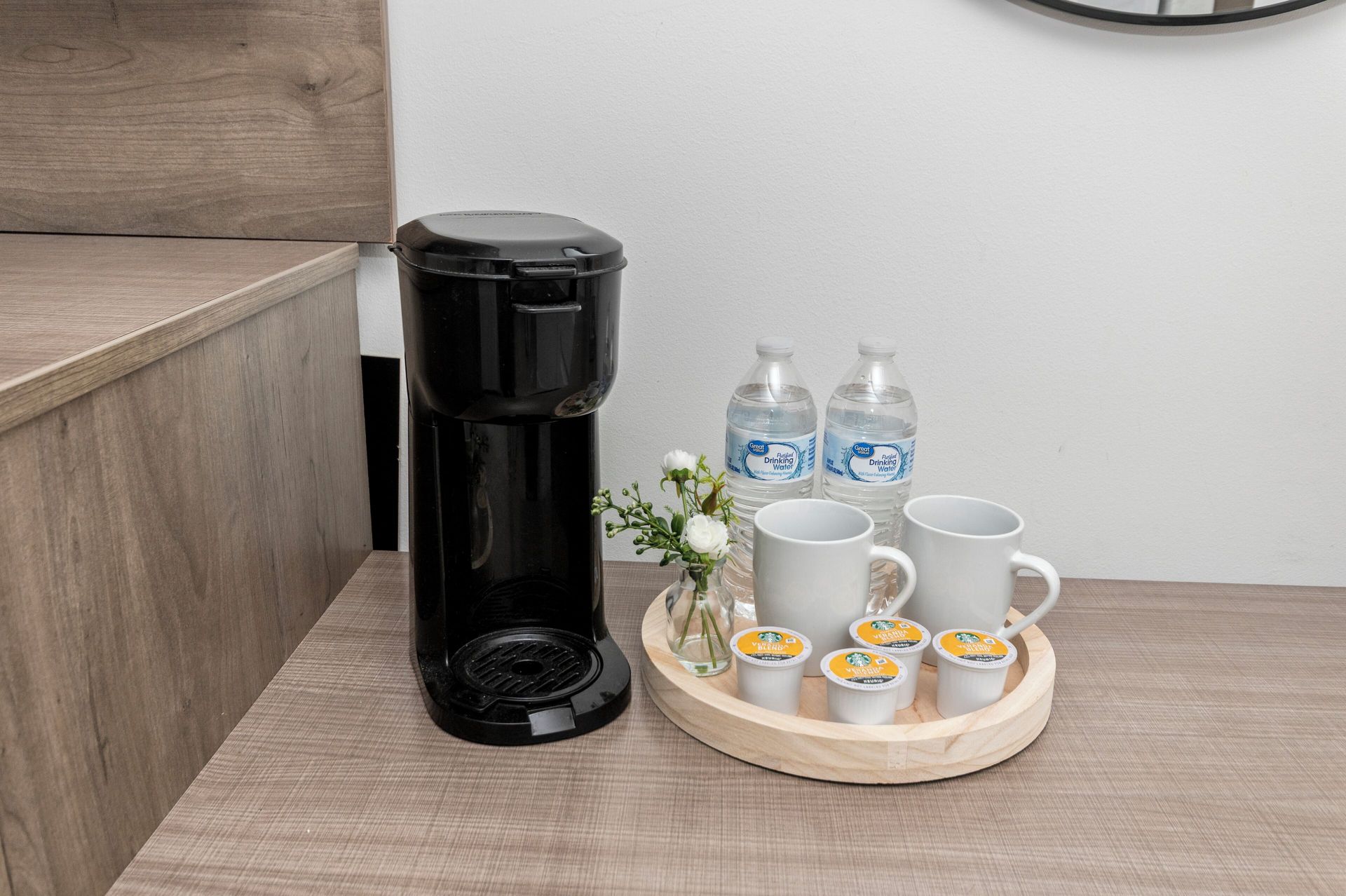 Coffee maker with mugs, bottled water, and snacks on a tray beside a sofa in a living room