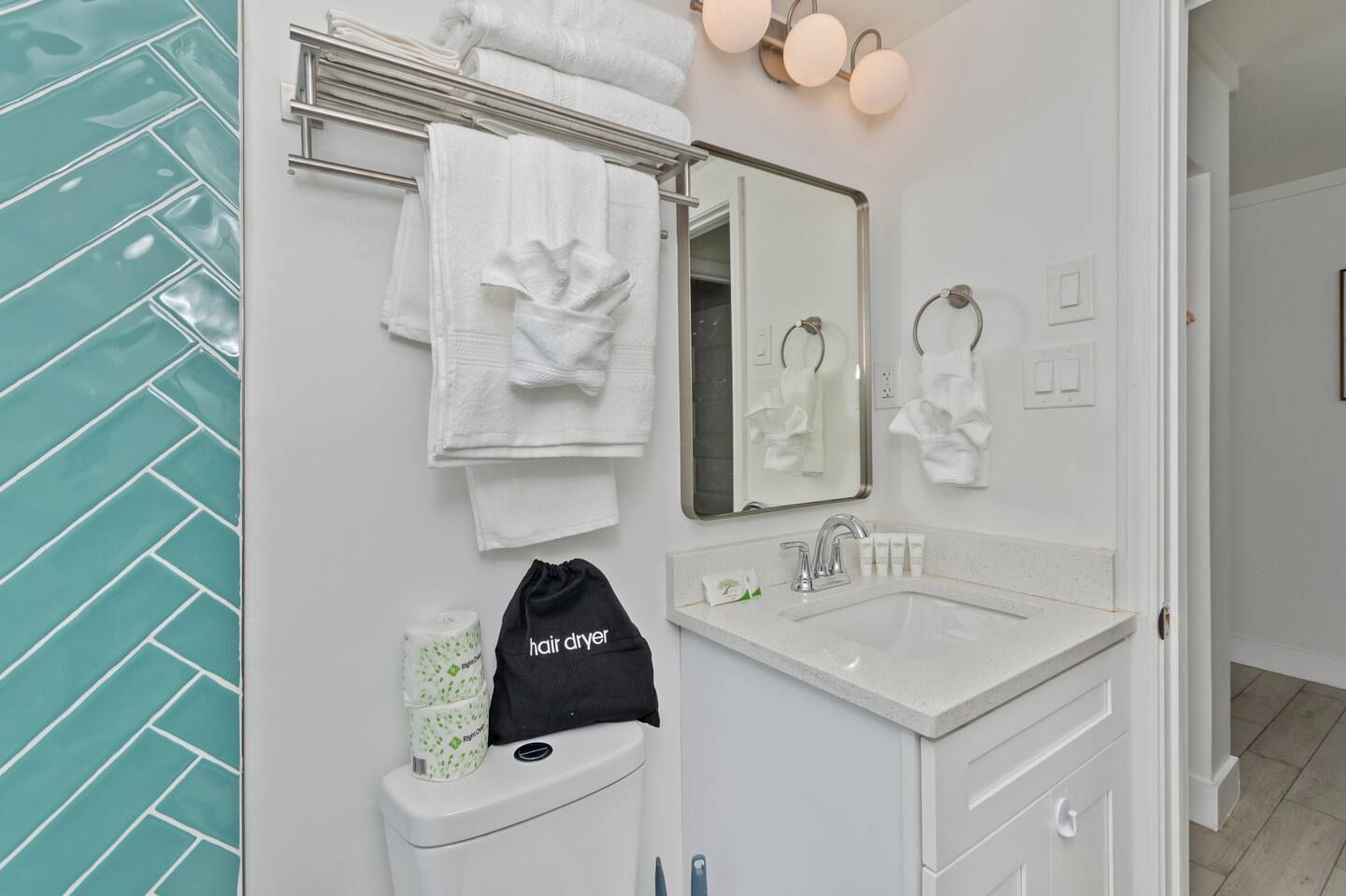 White bathroom vanity with mirror, towels, and teal tile accent wall