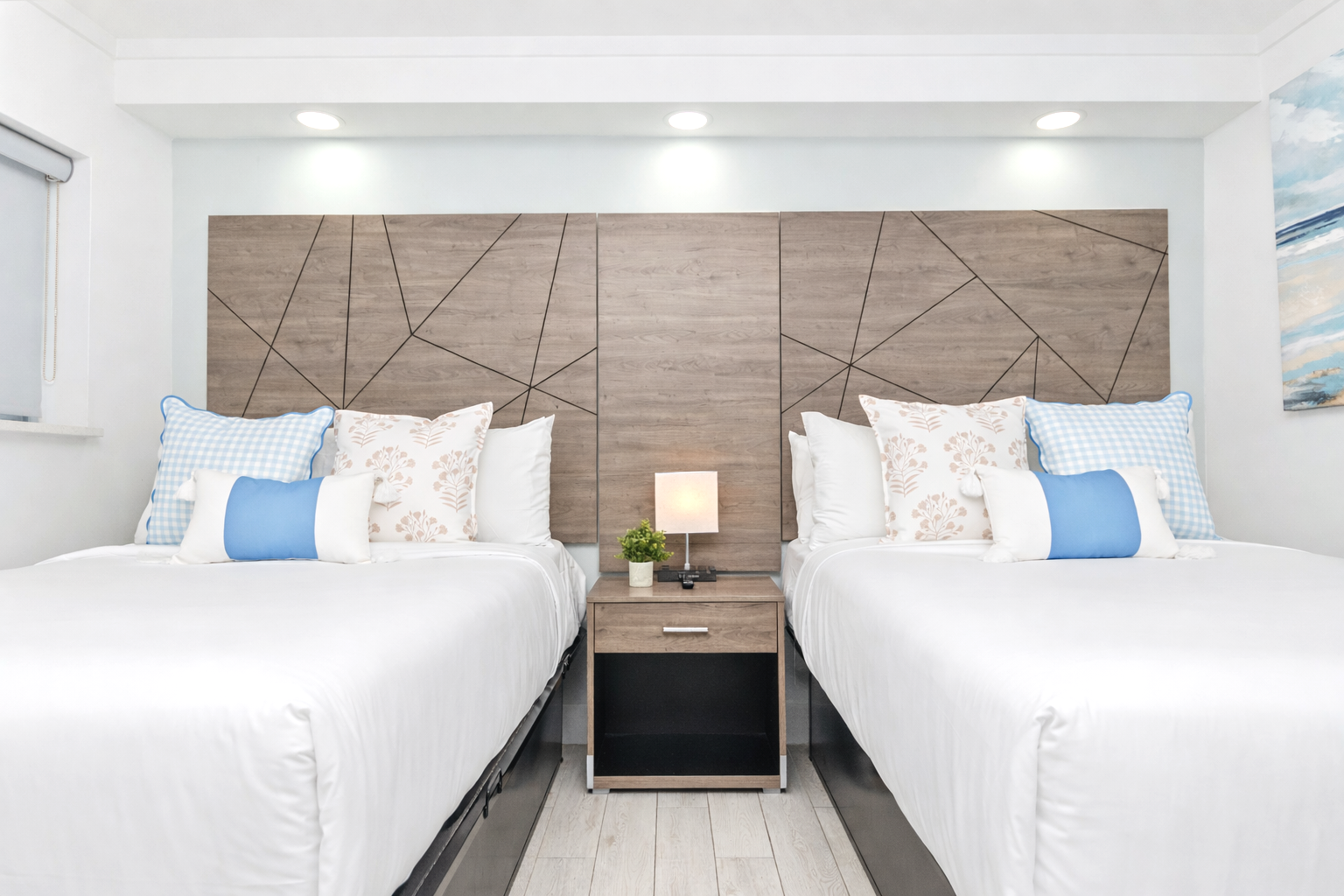 Modern twin bedroom with two white beds, blue pillows, and a wooden headboard accent wall