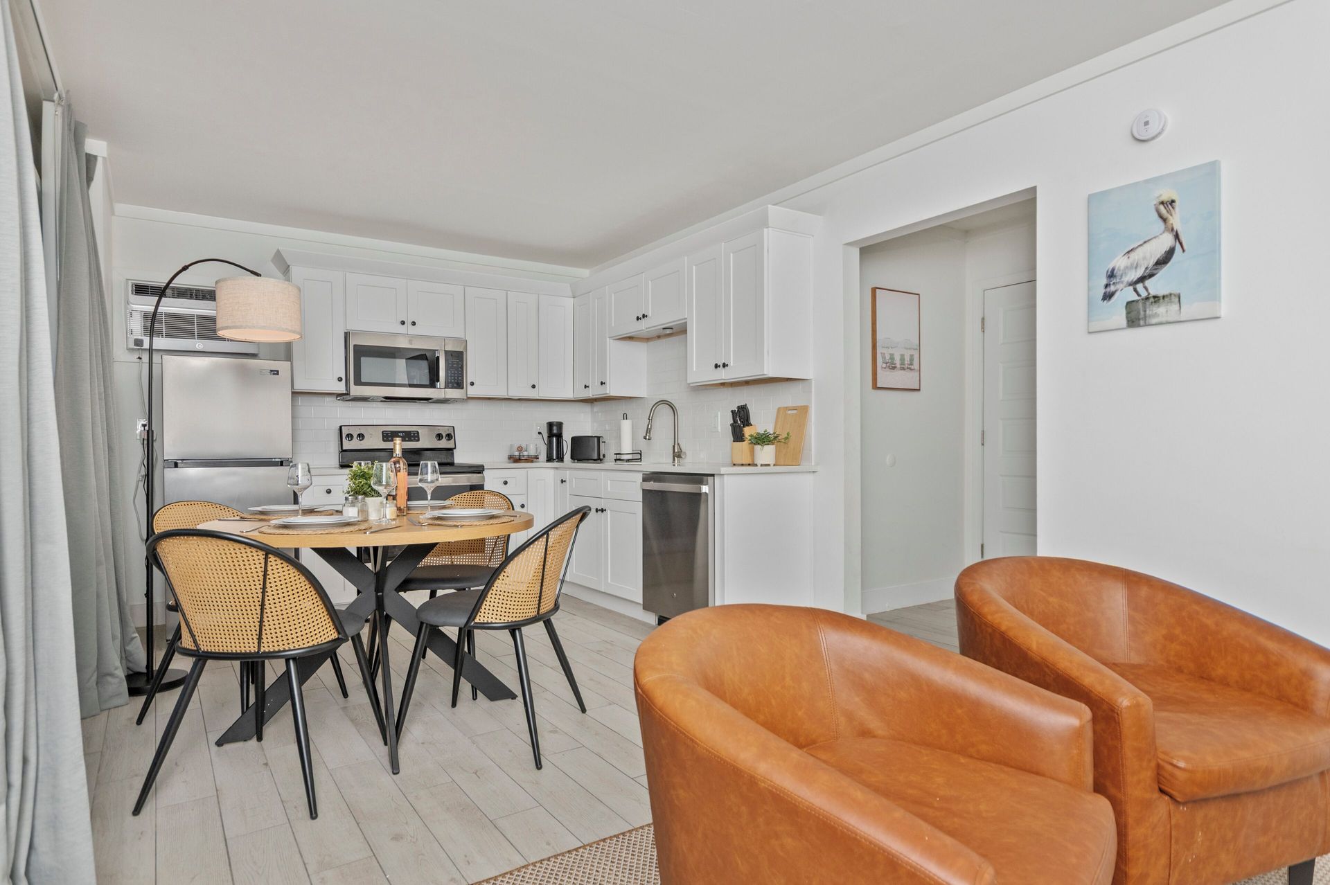 Bright modern kitchen and dining area with white cabinets, black table, and orange chairs