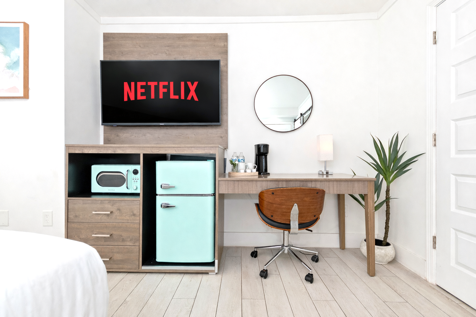 Small bedroom office with a mini fridge, desk, chair, and TV showing Netflix on the wall