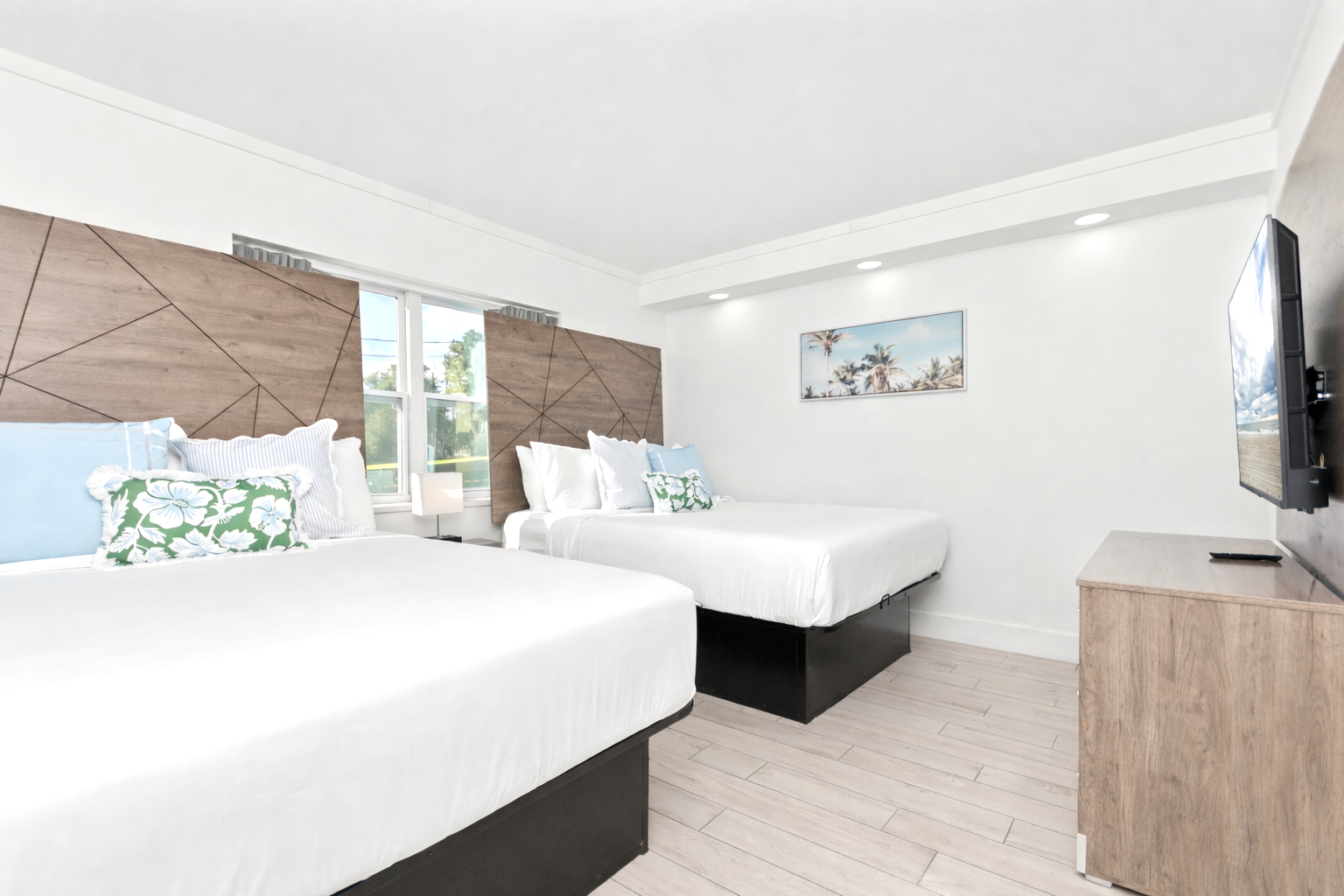 Bright modern hotel room with two white beds, wood accents, and wall art