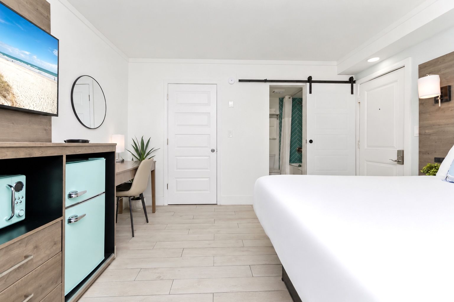 Bright modern bedroom with white walls, sliding barn door, desk, and neatly made bed