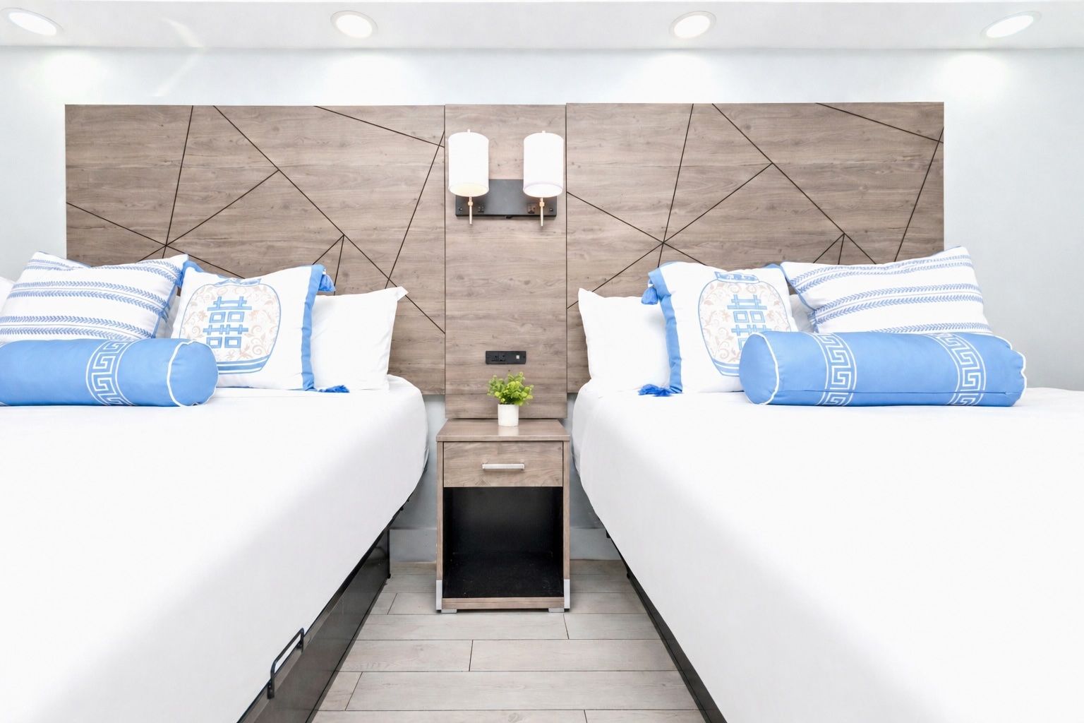 Bright bedroom with two twin beds, blue and white bedding, and a small nightstand between them.