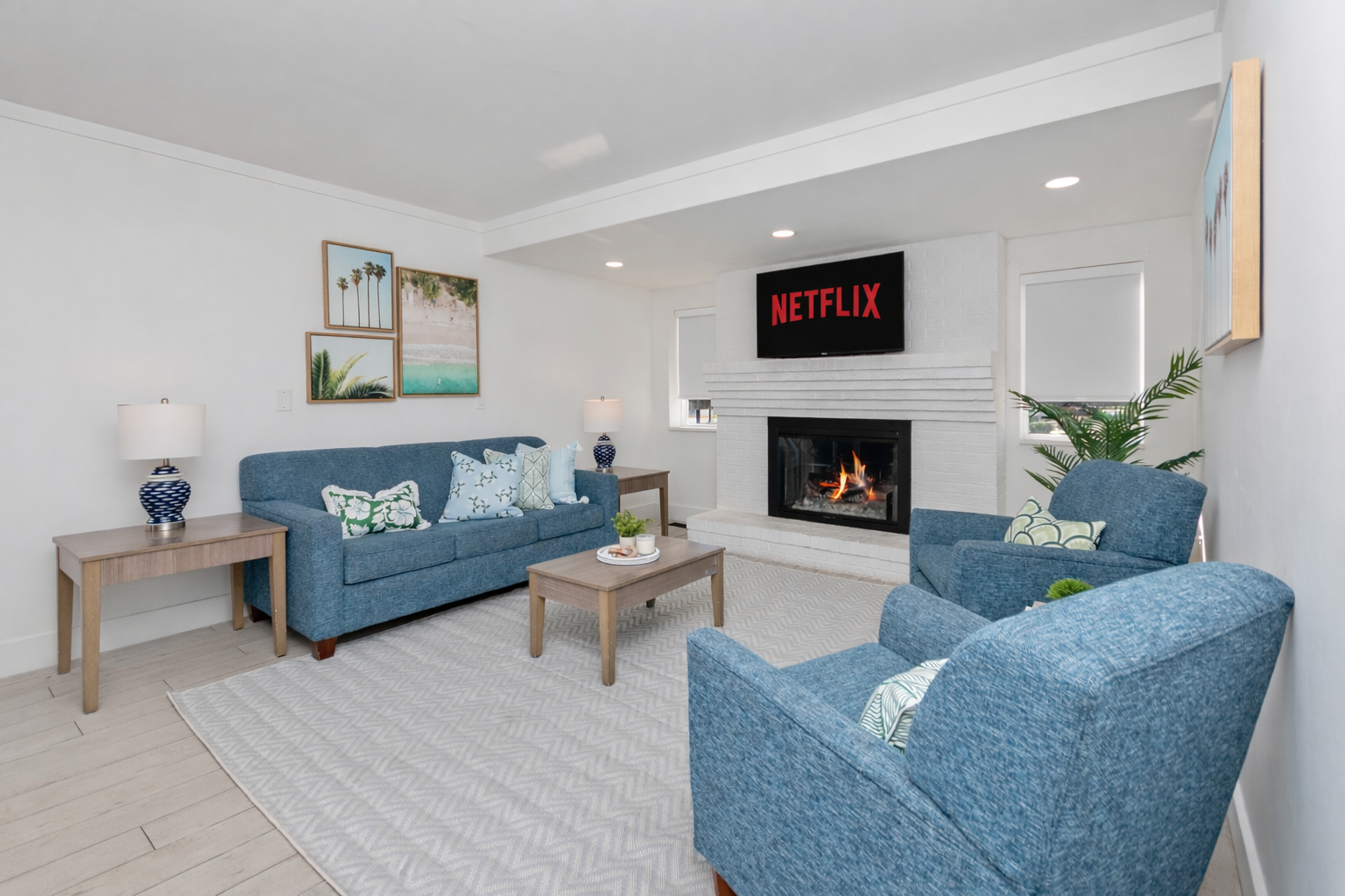 Bright living room with blue sofas, fireplace, and wall-mounted TV displaying Netflix