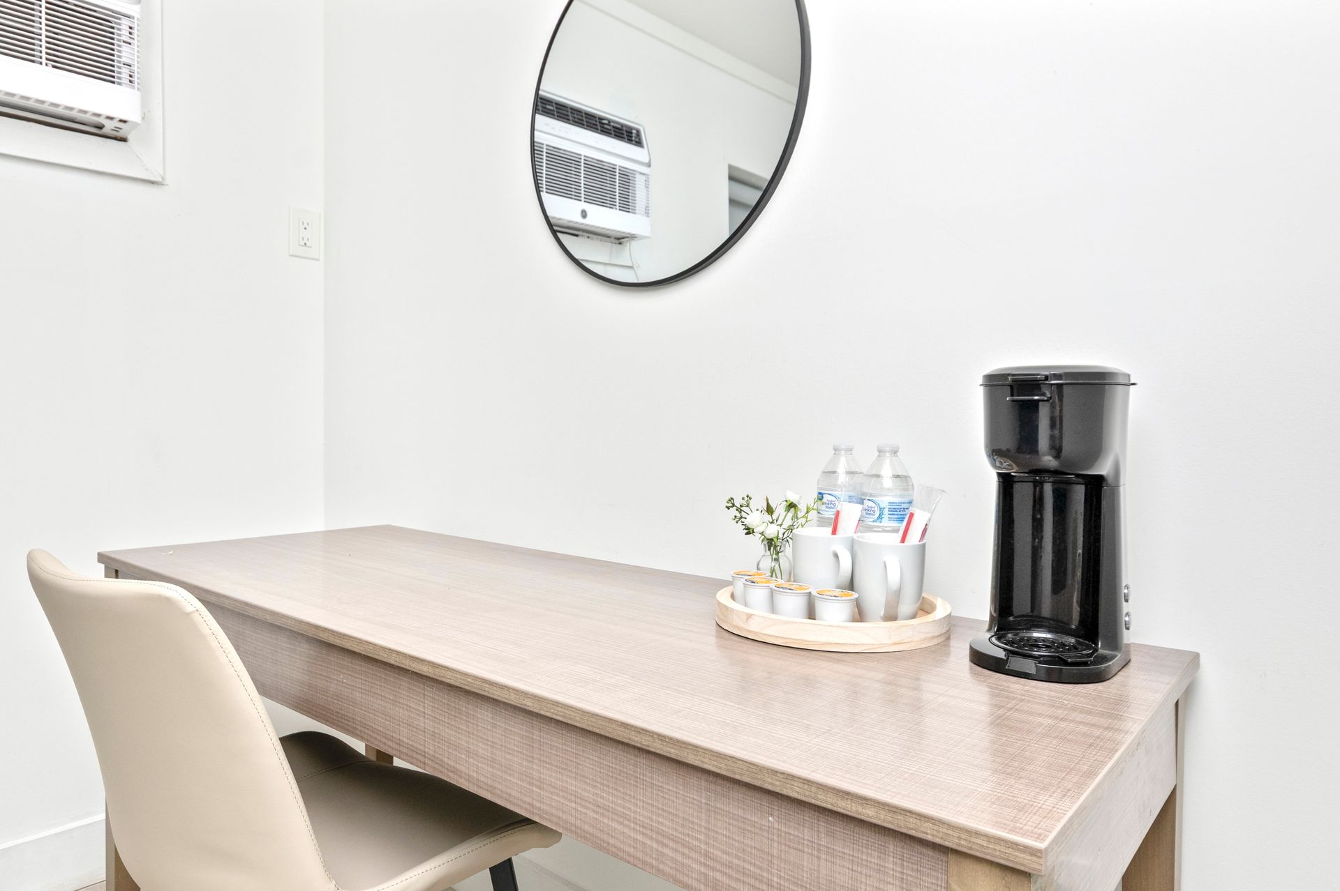 Minimal office table with beige chairs, round mirror, and a coffee machine on the right