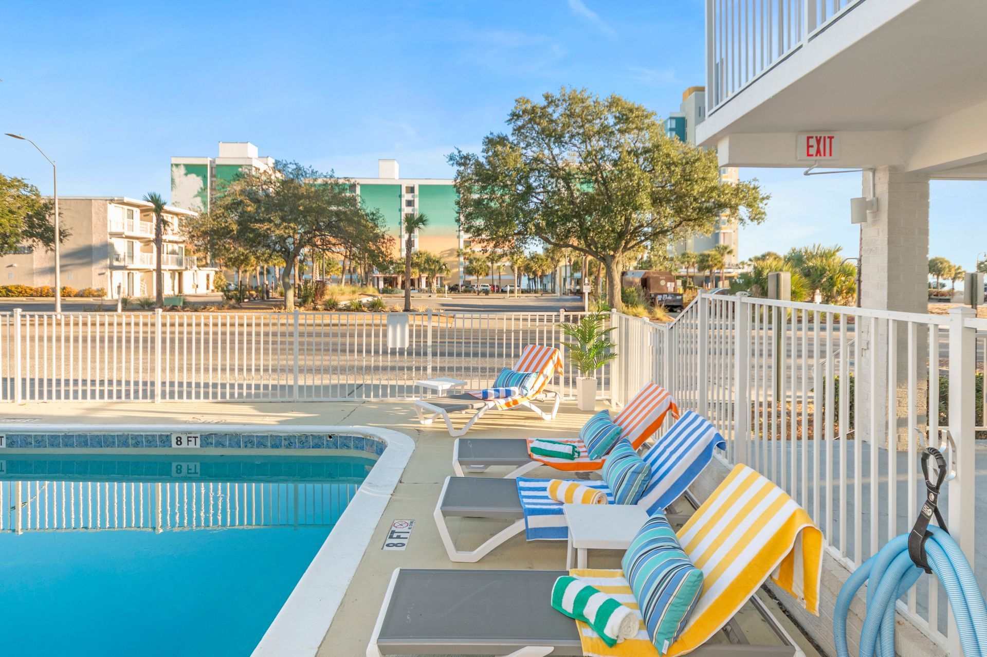 Poolside lounge chairs with striped towels beside an outdoor swimming pool and fence