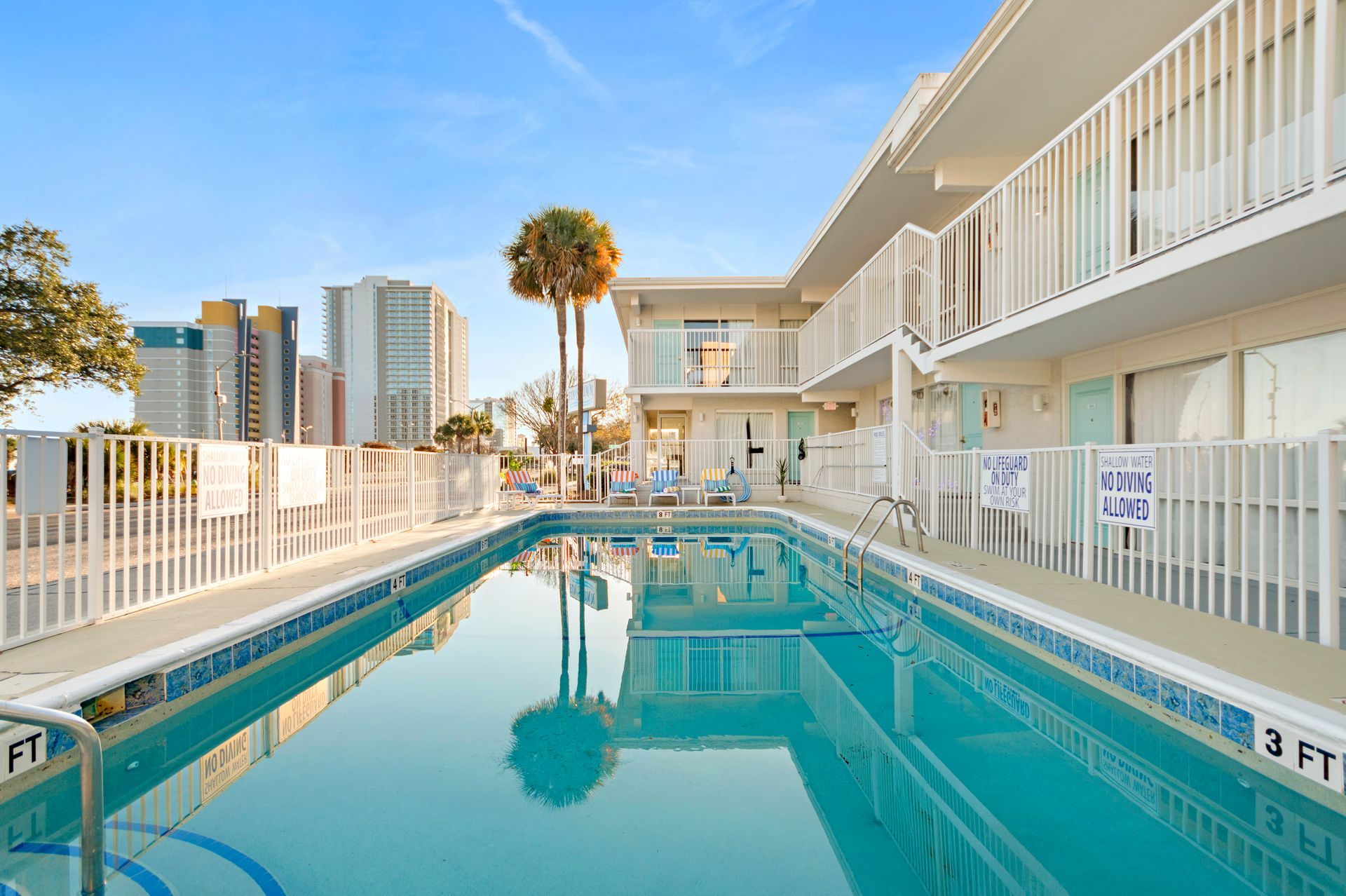 Outdoor swimming pool beside a white apartment building, with city skyline in the background