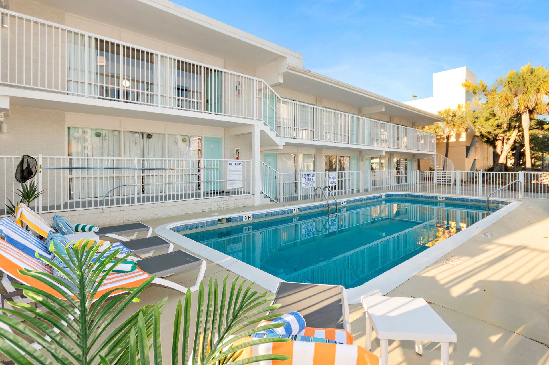 Outdoor hotel pool with turquoise water, lounge chairs, and balconies in bright sunlight