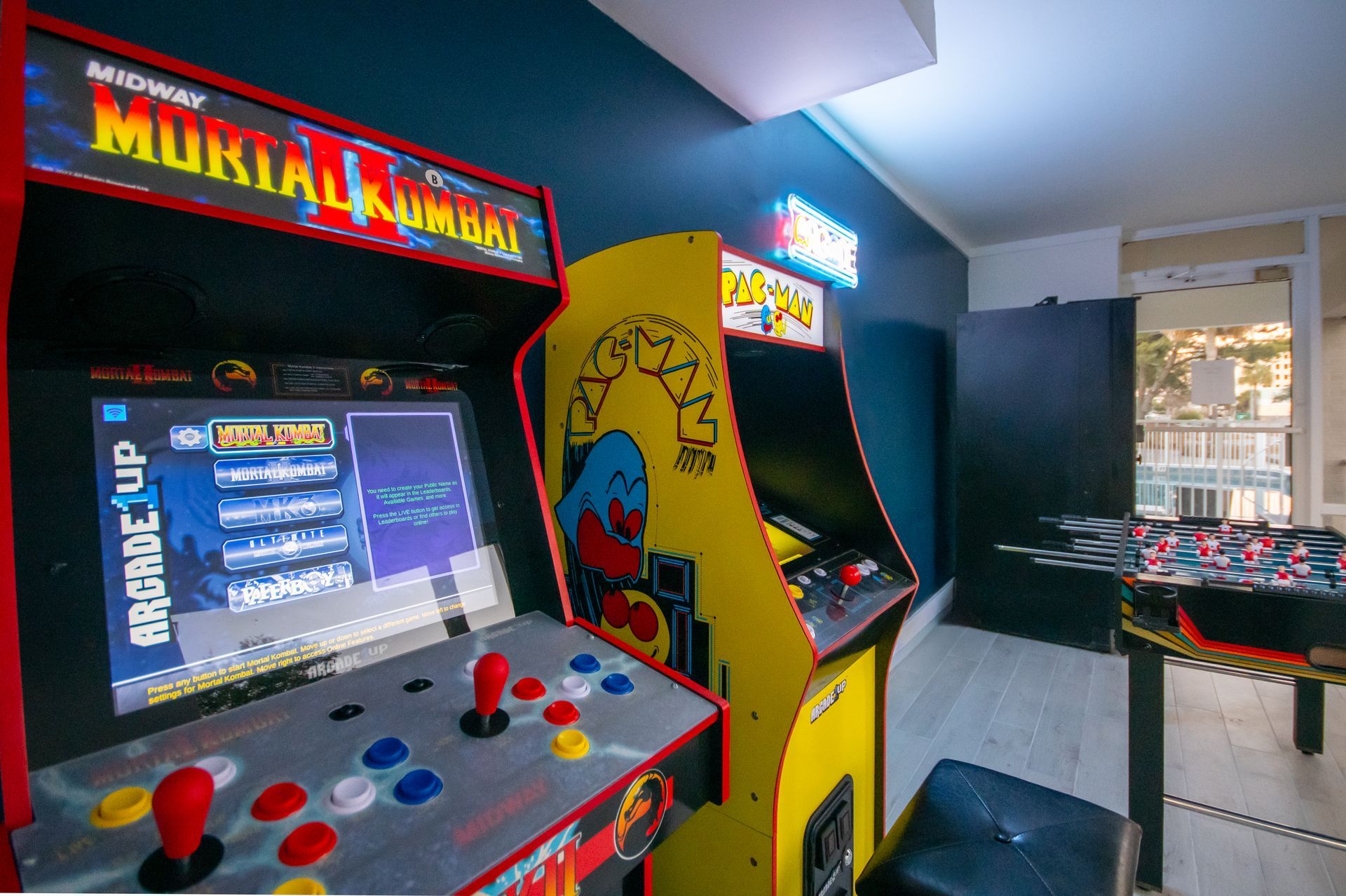 Arcade with colorful Mortal Kombat and Pac-Man arcade cabinets and a foosball table nearby