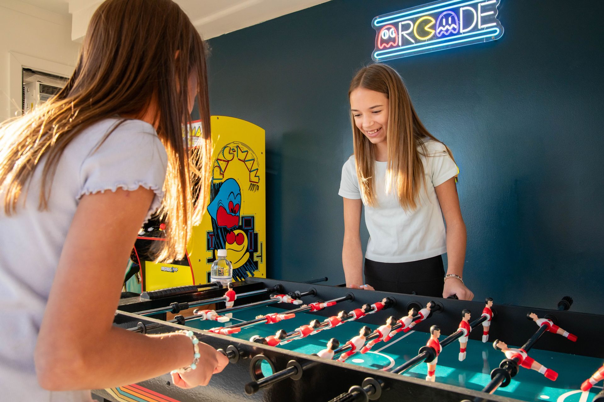Two people playing foosball in a bright room with an arcade sign on the wall