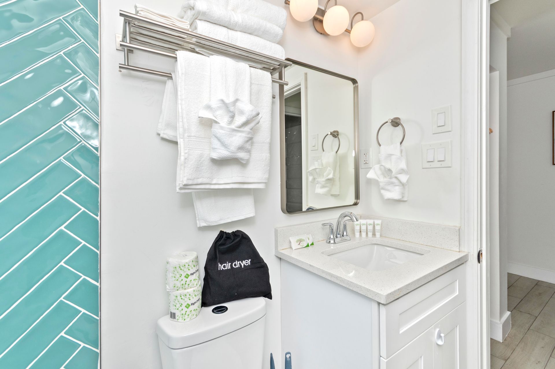 Bathroom with white vanity, towels, and turquoise tiled shower.