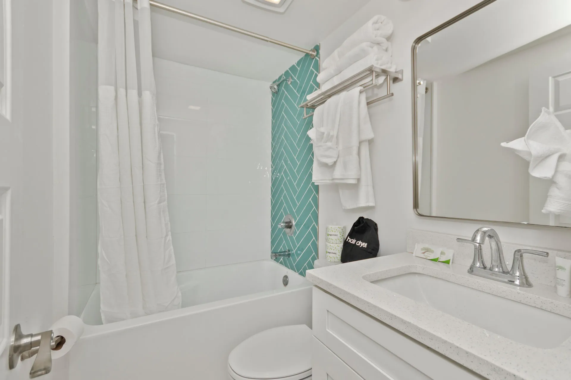 Bright white bathroom with a tub, shower curtain, vanity, and turquoise mosaic accent wall