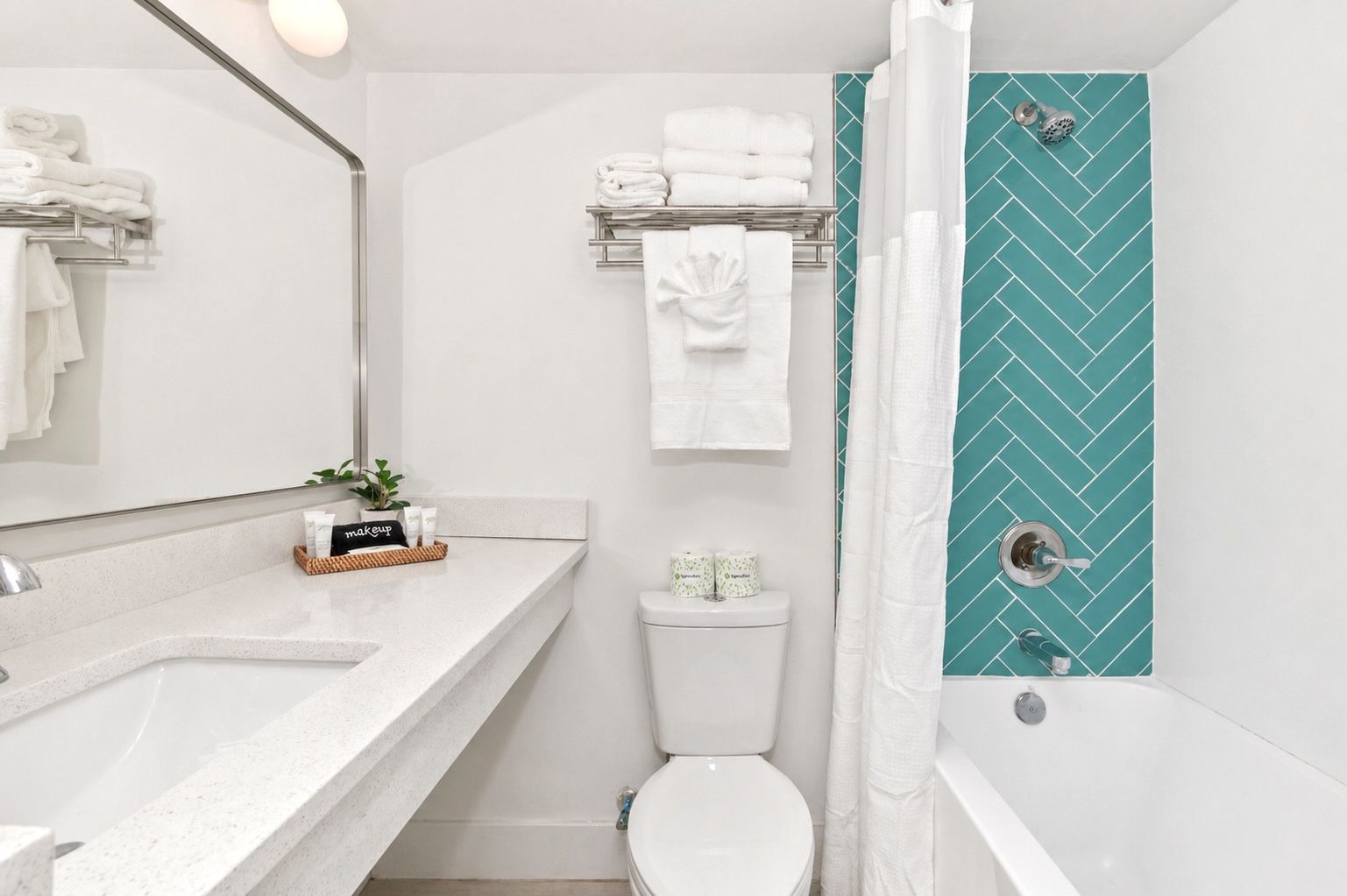 A bright white bathroom with a turquoise herringbone tile shower and a white vanity.