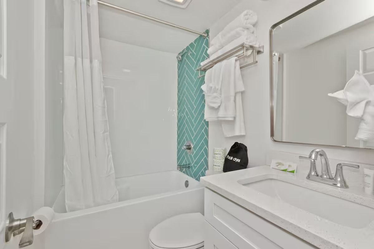 Bathroom with white fixtures, teal tile accent, and towels.