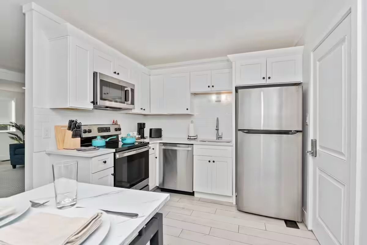 Bright white kitchen with stainless steel appliances and a small dining table by the window