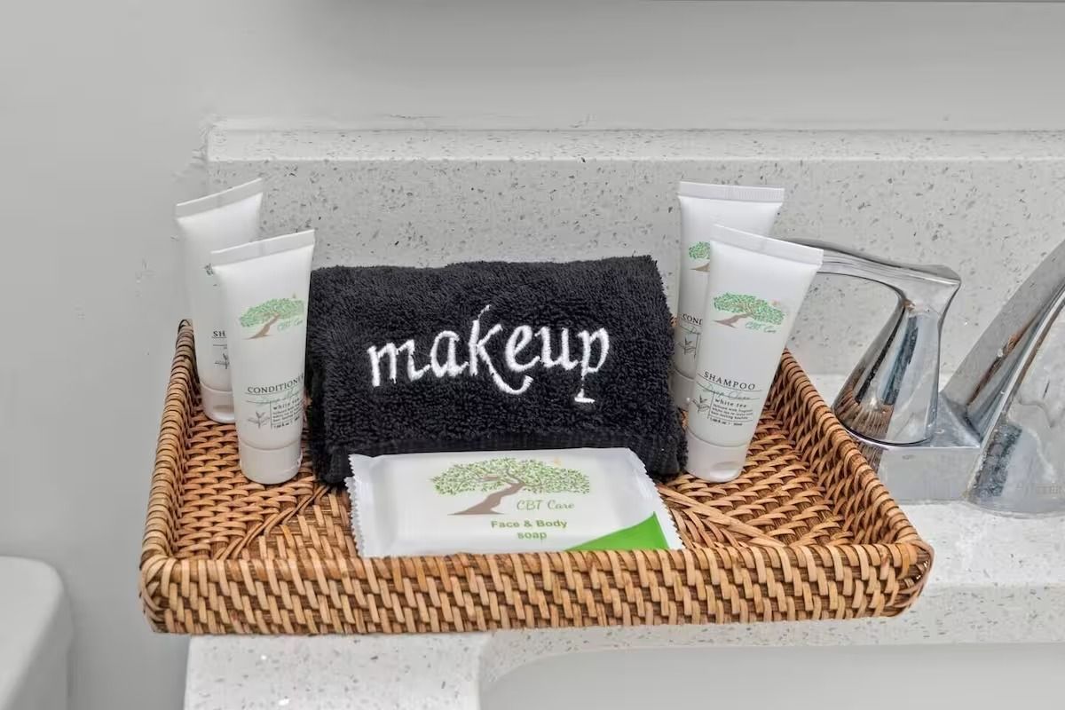 Wicker tray with toiletries: lotions, soap, a black towel embroidered 