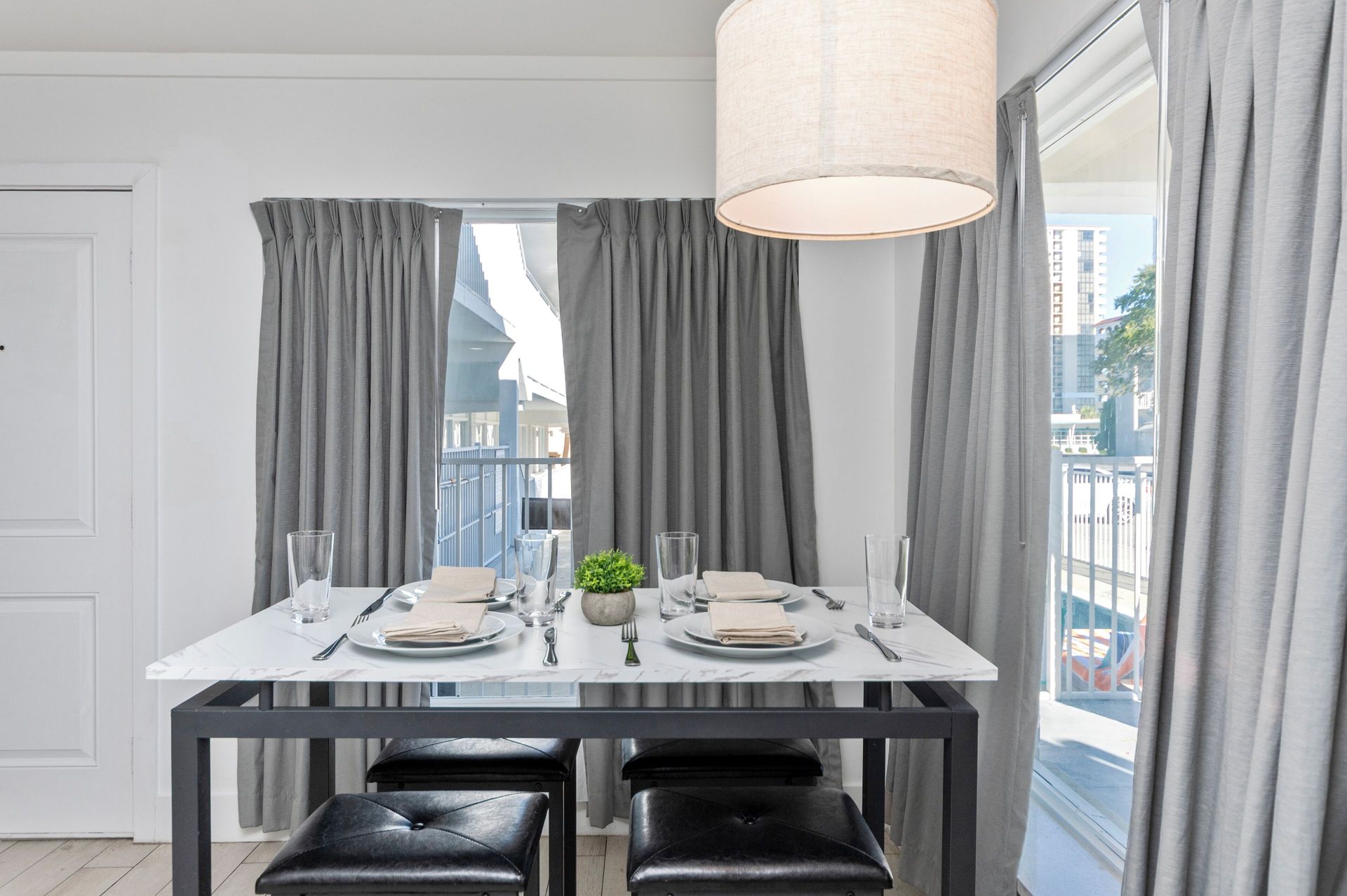 Modern dining room with a set table, black chairs, gray curtains, and large windows overlooking a balcony.